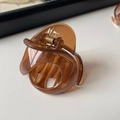 Détail de la pince à cheveux en résine ambre translucide avec ressort en métal doré brillant - Marron