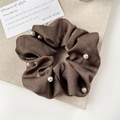 Detail of coffee brown satin scrunchie with elegant pearl accents on beige fabric - Brown