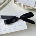 Dettaglio di un fermaglio per capelli a fiocco in raso nero con perle su piatto bianco - Stile Nodo a Fiocco