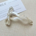 Close-up of pearlescent bow hair fork with wavy design on beige textured fabric - Mermaid White