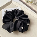 Dettaglio ravvicinato di uno scrunchie in raso nero con perle bianche su un vassoio - Nero
