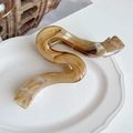 Macro-opname van gemarmerde amberkleurige haarklem met gouden metalen veer op wit bord - Koffie Gradiënt