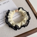 Detail of a beige elastic scrunchie with black lace trim and a resin bead on a tray - Cream White with Black Edge