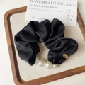 Dettaglio di uno scrunchie in seta nera con perle bianche e una targhetta in metallo oro - Nero