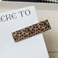 Detailansicht der Haarspange mit Leopardenmuster auf einer Karte mit Textilhintergrund - Leopardenmuster Rechteckig