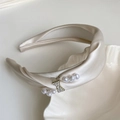 Nahaufnahme des champagnerfarbenen Satin-Haarreifs mit Strass-Schmetterling und weißen Perlen - Gebrochenes Weiß