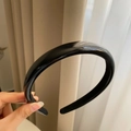 Dettaglio di un cerchietto minimalista in pelle sintetica nera con finitura lucida - Nero