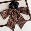 Detail eines Leopardenmuster-Haargummis mit goldener Wings-Plakette auf Leinentablett - Leoparden-Scrunchie-Stil