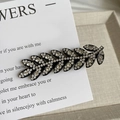 Détail macro d'une barrette en forme de feuille avec cristaux sur base noire - Argenté