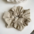 Close-up of beige pleated chiffon scrunchie with elegant metal logo charm detail - Off White