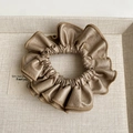 Detailed view of bronze faux leather ruffled scrunchie with metallic finish on a tray - Khaki Hair Tie