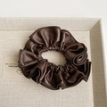 Detailed view of dark brown leather scrunchie with pleated texture on a beige tray - Coffee - Scrunchie