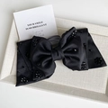 Close-up of black satin bow hair clip with sparkling crystals on a fabric display tray - Black
