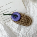 Dettaglio macro di un fermaglio per capelli in maglia con bottone viola e cordino verde - Filato di Caffè Bottone Viola