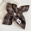 Dettaglio dell'elastico per capelli a quadri marroni con etichetta orso su fondo beige - Scozzese Marrone - Stile Nastro