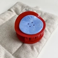 Detail view of a vibrant red hair claw clip with a blue marble-patterned button on fabric - Red