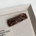 Close-up of brown knit BB hair clip on a beige fabric tray in a warm autumn aesthetic - Coffee Bar