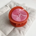 Close-up of orange acrylic hair claw clip with unique pink marble button decoration - Orange Red