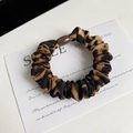 Primo piano di elastico in raso leopardato con fibbia in plastica marrone su carta - Leopardo Caffè Scuro