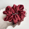 Close-up of premium satin scrunchie in burgundy red on a decorative white dish - Red