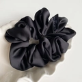 Detailed view of black satin scrunchie with woven label on a white shell tray - Black