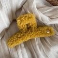 Close-up of ginger plush hair claw with a gold oval Korea logo on beige linen background - Yellow