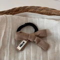 Detailaufnahme des braunen Strick-Schleifen-Haargummis mit Nice-Label auf Stoffhintergrund - Beige