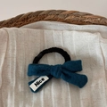 Detail von blauem Woll-Schleifen-Haargummi mit Nice-Etikett auf Leinen und Weidenkorb - Blau