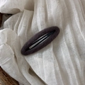 Detailed macro view of dark brown felt fabric oval BB hair clip on soft white textile background - Dark Brown