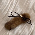 Close-up of soft brown plush hair clip featuring a black bow and gold brand plaque - Yellow Coffee