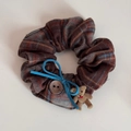 Detalle de coletero a cuadros con lazo azul, botón de madera y un pequeño oso colgante - Tela Gris Marrón Lazo Azul Oso Scrunchie