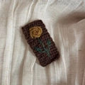 Makro-Detail einer handgehäkelten Haarspange mit Rosenmuster auf braunem Strickgrund - Hellkaffee