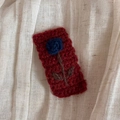 Detail einer handgestrickten Haarklammer mit burgunderroter Basis und blauer Rose - Rot