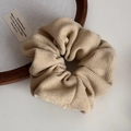 Close-up of a light coffee knitted scrunchie with textured fabric on a wooden tray - Textured Scrunchie / Yellow
