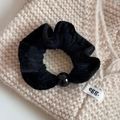 Detailed view of a plush black hair scrunchie with round bead on a textured knit background - Black