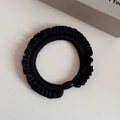 Close-up of black ruffled elastic hair tie with a decorative bead on cream surface - Black
