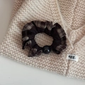 Nahaufnahme des Vintage Karo-Haargummis mit schwarzer Perle auf gestricktem Hintergrund - Braun