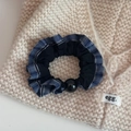 Nahaufnahme von blauem Karomuster-Haargummi mit schwarzer Perle auf Strickware - Blau