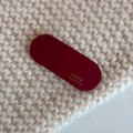 Detail of burgundy oval acetate hair clip with golden handmade logo on knit fabric - Burgundy