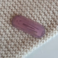 Macro shot of purple oval acetate hair clip with gold logo on beige knit texture - Purple Pink