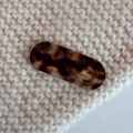 Dettaglio di fermaglio ovale in acetato tartarugato su sfondo in maglia beige - Tartarugato
