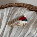 Dettaglio del fermaglio natalizio lavorato a maglia con bordo dorato e perla su tessuto beige - Cappello di Natale