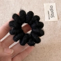 Gros plan d'un élastique à cheveux en peluche noire tenu en main avec lumière douce - Noir