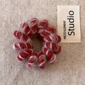 Detail van een rode pluche spiraal haarelastiek met zachte textuur op een beige stoffen - Rood