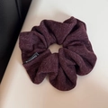 Detailed macro view of deep purple knitted fabric scrunchie with woven texture and side label - Purple