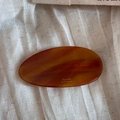 Macro shot of an amber acetate oval barrette with French lettering on white linen - Caramel color
