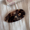 Detailed close-up of tortoise shell oval hair clip with gold lettering on linen fabric - Tortoise