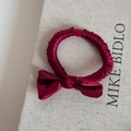 Detalle de coletero con lazo de satén rojo oscuro y textura plisada sobre tela beige - Estilo Lazo / Rojo Año Nuevo