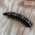 Close-up of black and white checkered banana hair clip on beige textured fabric - Gray