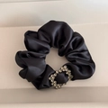 Detailed close-up of a black satin hair scrunchie with a sparkling heart rhinestone charm - Square Rhinestone Scrunchie